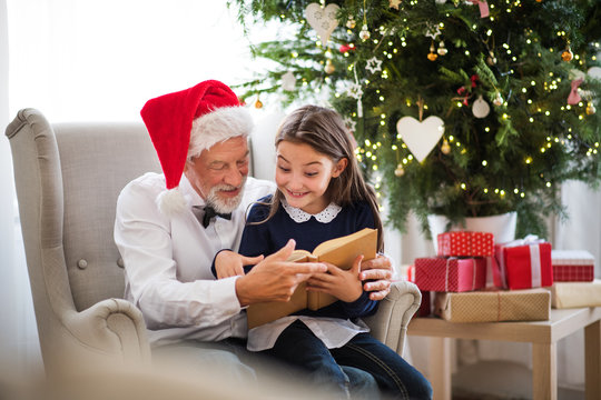 A small girl and her grandfather with Santa hat and a book at Christmas time.