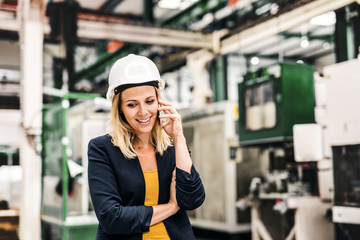Fototapeta na wymiar A portrait of an industrial woman engineer on the phone, standing in a factory.