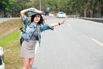 Young asian traveler with backpack waiting for car on the road while traveling during holiday vacation