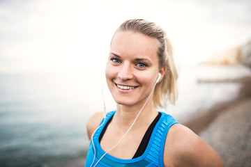 Young sporty woman runner with earphones standing on the beach outside.