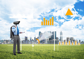 Camera headed man standing on green grass against modern cityscape