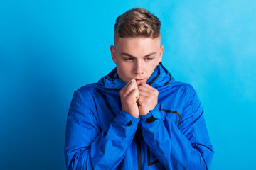 Portrait of a young man with blue anorak in a studio, feeling cold. Copy space. © Halfpoint
