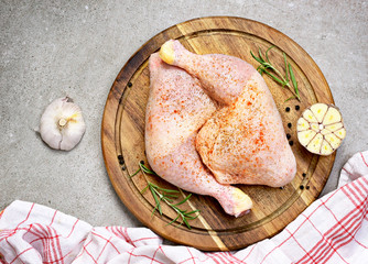 Delicious raw chicken legs or drumsticks on a wooden cutting board. Rustic preparation scene with garlic and raw meat.