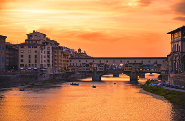 colorful buildings, bridge Ponte Vecchio and water reflections in warm sunset on river Arno with small boats in florence, italy