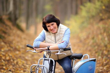 Obraz premium The girl on a bike from the rental in the forest. Beautiful young woman posing for the camera in the autumn forest. 