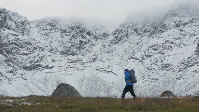 A man with a backpack, alone, traveling in the mountains. It goes along high snowy peaks.