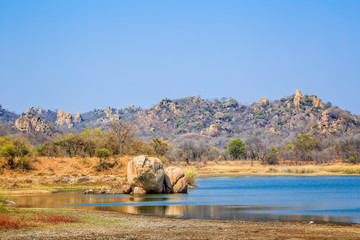 View of a lake surrounded by rocks, in Matobo National Park, Zimbabwe. September 26, 2016. - obrazy, fototapety, plakaty