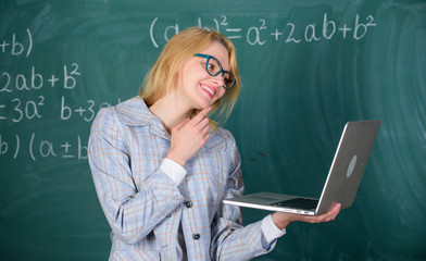 Woman teacher wear eyeglasses holds laptop surfing internet. Educator smart clever lady with modern laptop searching information chalkboard background. Learn it easy way. Online schooling concept