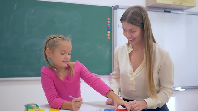 Individual education, Experienced tutor teaching smart girl at table near blackboard in classroom of Primary School