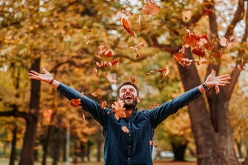 Fototapeten Young man throwing autumn leaves in the air © marjan4782
