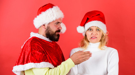 Man with beard and woman in santa hat on red background. Girl disgusted face celebrate christmas. Couple celebrate winter holiday christmas. Christmas masquerade or karnival concept