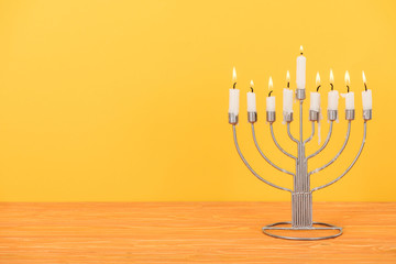 close up view of menorah with candles for hannukah holiday celebration on wooden tabletop isolated on yellow, hannukah concept