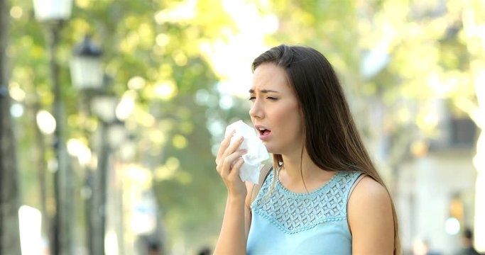 Ill woman sneezing covering mouth with a tissue in the street