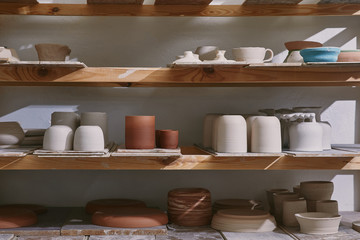 ceramic bowls and dishes on wooden shelves at pottery studio - obrazy, fototapety, plakaty