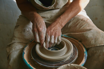 partial view of professional potter working on pottery wheel at workshop