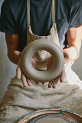 cropped image of professional potter in apron holding clay at pottery studio