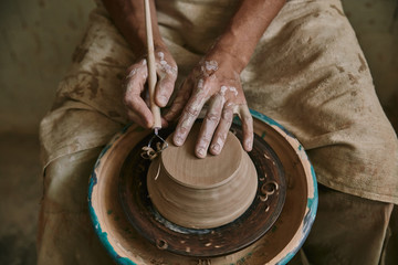 partial view of professional potter decorating clay pot at workshop