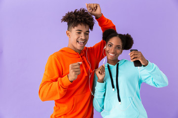 Photo of african american couple in colorful clothes dancing while listening to music together with...