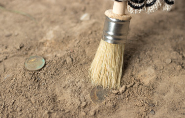  archeology female hand holds brush a tassel excavation of rare materials treasure hunt and archeology find rare  Gold coins in sand  - obrazy, fototapety, plakaty