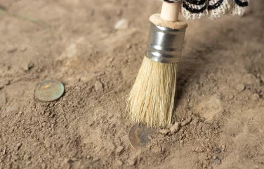Foto op Canvas  archeology female hand holds brush a tassel excavation of rare materials treasure hunt and archeology find rare  Gold coins in sand  © Ирина Абраменко