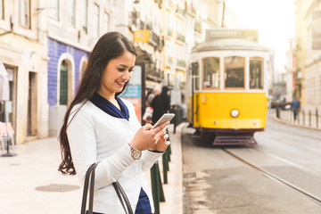 Woman tourist in Lisbon checking tram timetable on her smartphone - obrazy, fototapety, plakaty
