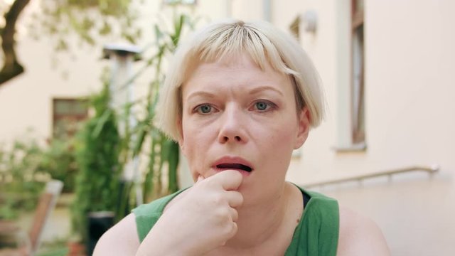 A pretty young blonde woman wearing a green dress sitting outside with a worried look on her face. Close-up shot