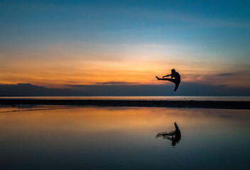 young athletic guy performing a flying kick during sunset on the beach