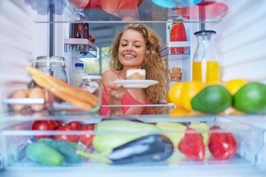  Woman taking gateau form fridge full of groceries. Unhealthy eating concept. Picture taken from the inside of fridge.