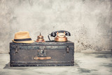 Vintage old classic travel trunk luggage with leather handles circa early 1900s, rotary telephone, hotel service bell and men's hat. Retro style filtered photo