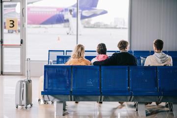 back view of young people sitting and waiting for flight in airport terminal