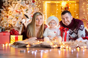 Happy family with a baby in a Santa Claus hat in a Christmas room in Christmas day.