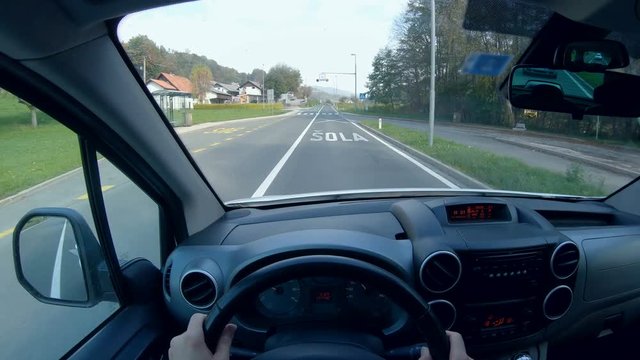 Driver POV of traveling through countryside village 4K. Driver point of view behind the car wheel in focus while driving through speed limited section.