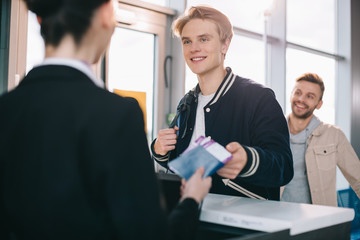 cropped shot of smiling young man giving passport to worker at check-in desk in airport