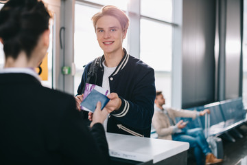 smiling young man giving passport to worker at check-in desk in airport