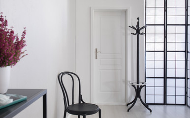 Black wooden chair in white corridor of elegant apartment, real photo with copy space on the white wall