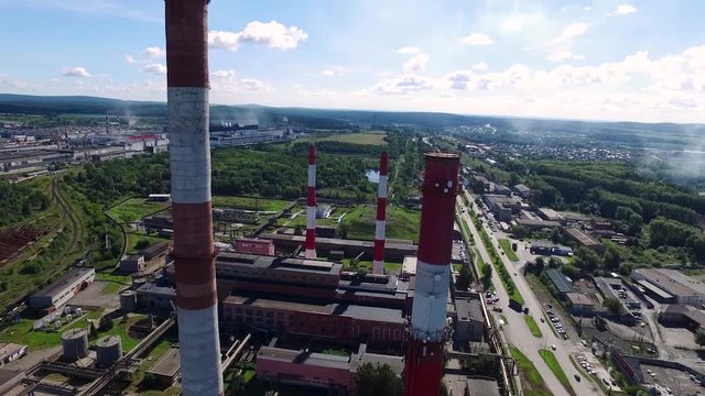 Cityscape with industrial building plant with three tall red and white industrial pipes over clear cloudless blue sky on sunny day. Footage. Top view near of white-red chimneys of plant. Concept of