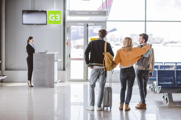 back view of young friends going to check-in desk in airport