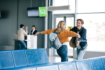 happy young couple with backpacks hugging in airport terminal