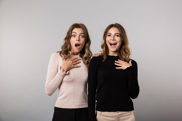 Image of two surprised women wondering while posing together, isolated over gray background