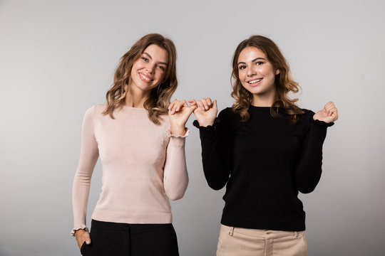 Image of two young women smiling and hooking each others little fingers in conciliation or friendship, isolated over gray background