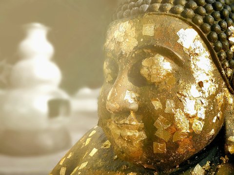 Close up of gold leaves on surface of smiling Buddha statue with flare light and blur background in art of religion and Thai traditional concept