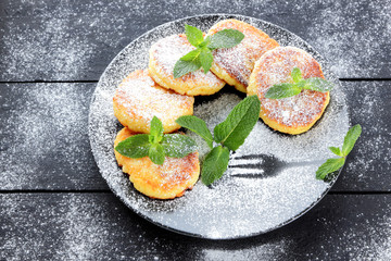 Cottage cheese pancakes with fresh mint sprinkled with powdered sugar. Syrniki on dark wooden boards. Healthy food for breakfast. Dish of milk products. Copy space