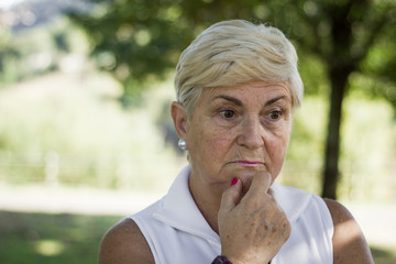 Portrait of mature woman concerned with hand on chin looking pensive in the park. Senior lady with pessimistic look. Sad, menopause symptoms, melancholic concept