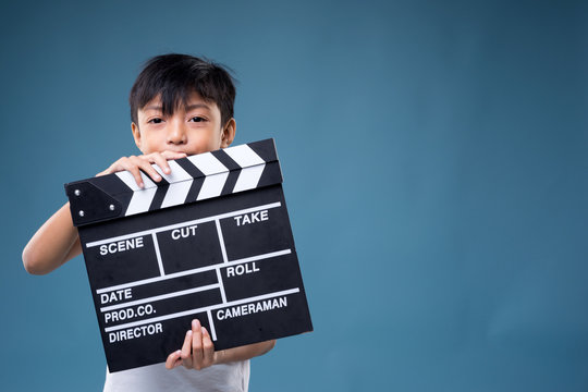 An Asian boy poses with a movie clapperboard on blue background