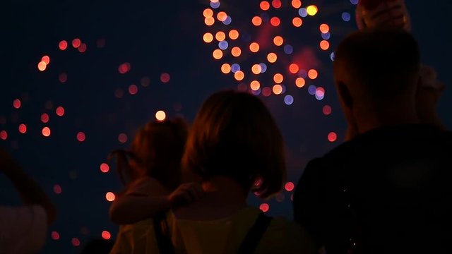 A young family with a baby in their hands are standing watching the salute in the night sky. slow motion, 1920x1080, full hd