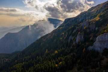 Aerial photography over big mountain forest. Sunset over the forest. Foggy valley at the sunrise. Golden hour over the forest with mist. Beautiful aerial landscape. Drone shots over the foggy forest. 