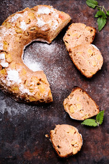 Homemade rustic Spicy Apple Bundt Cake sprinkled with icing sugar on old rusty metal background. Sliced. Top view