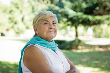 Beautiful mature woman portrait in the park resting chin on hand with her mind somewhere else. Senior blonde lady with optimistic expression, positive, dreamer, thoughtful concept