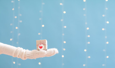 Person holding a Christmas gift box on a shiny light blue background