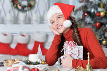 Portrait of beautiful happy girl in Santa hat sitting with Christmas present